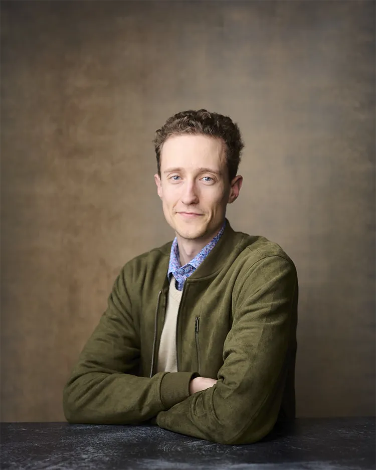 Professional business portrait of young man in olive green jacket smiling warmly at portrait studio